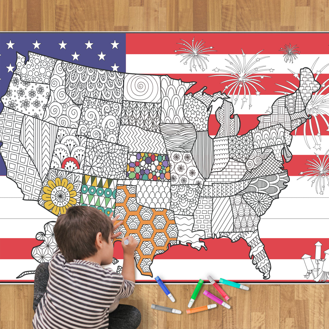 boy sitting down and coloring a giant coloring page that has a USA map with USA flag in the background.